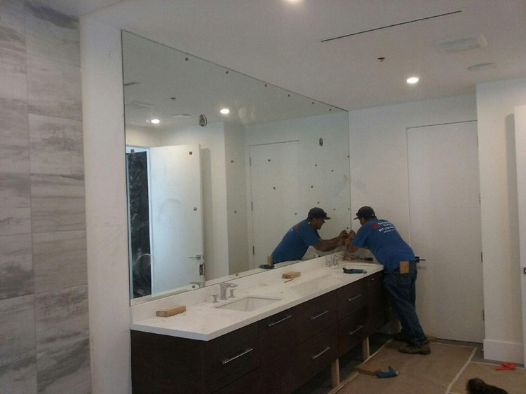 A custom vanity mirror with light fixture and outlet cutouts during the installation process.